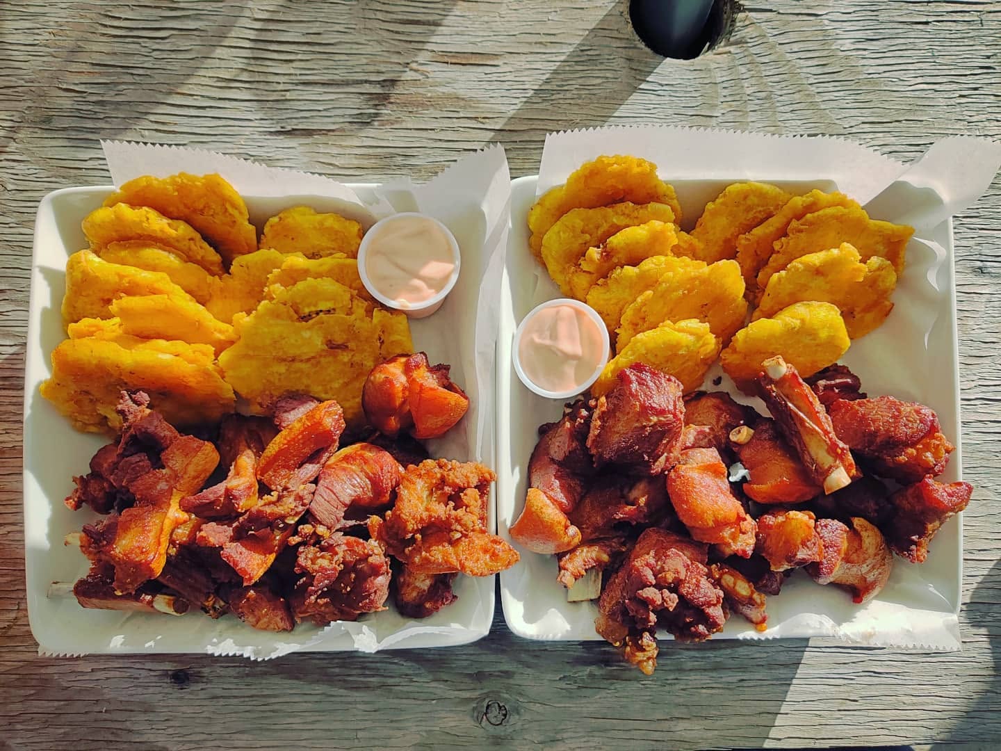 Dos bandejas con carne frita, tostones y mayoketchup sobre una mesa de madera