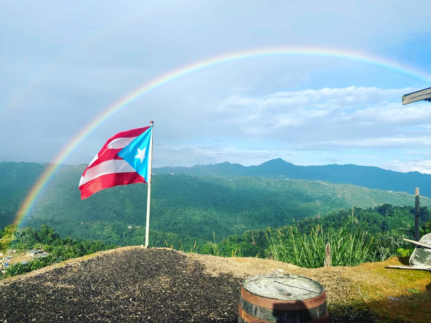 Bandera de Puerto Rico en la cima del cerro con un arcoíris sobre la montaña