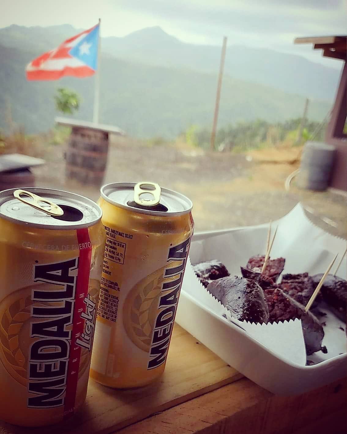 Morcilla criolla en pedazos con dos latas de Medalla y la bandera de fondo